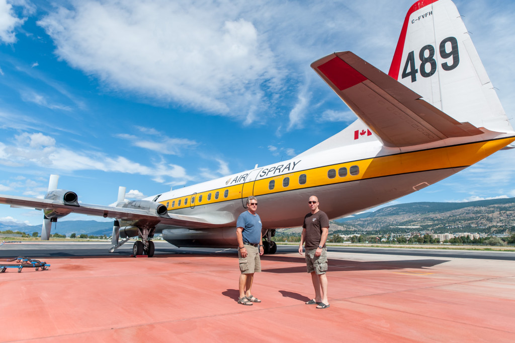 Ben Moerkoert (left) Air Attack officer, and Jeff Pulkinen, co-pilot, stand on the tarmac below an air tanker made from a converted Electra L188, a turboprop plane first introduced in 1957. The tarmac is red from spilled fire retardant. (Richard McGuire photo)