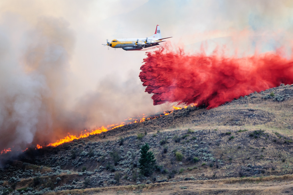 A bomber plane drops red fire retardant on a strip of land between approaching flames and a large house. With this one drop, it appeared to stop the flames from gaining on the house. The brush fire occurred Aug. 19, 2013 night near Spotted Lake west of Osoyoos. (Richard McGuire photo)